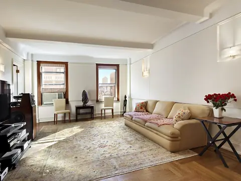 A living room with a beamed ceiling, panelled cream walls with sconces, a sofa and a large rug on a herringbone floor