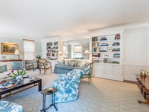 A living room with white built-in bookshelves around a mirrored niche, panelled walls and blue and white floral armchairs